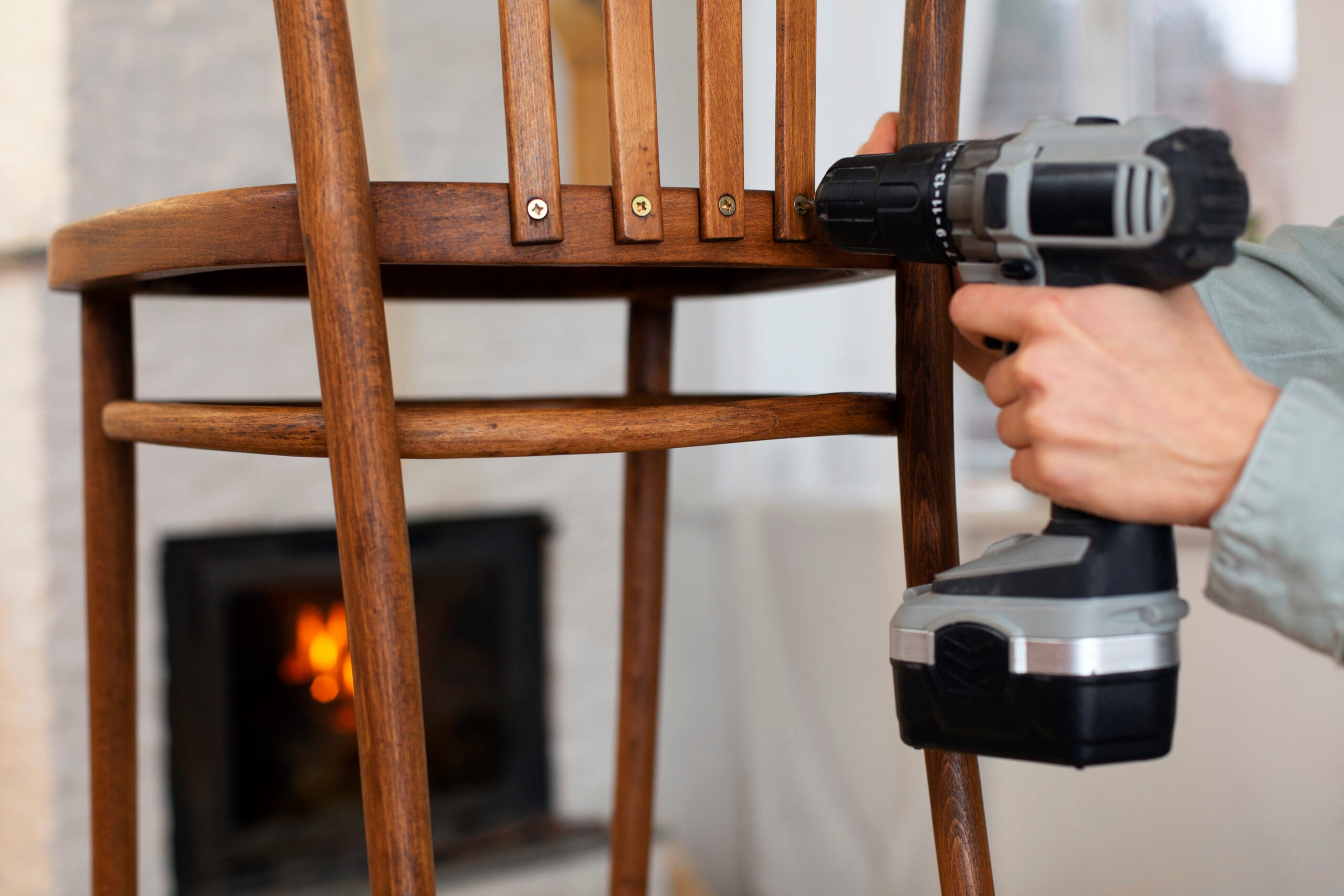 Woman repairing wooden chair with drill.
